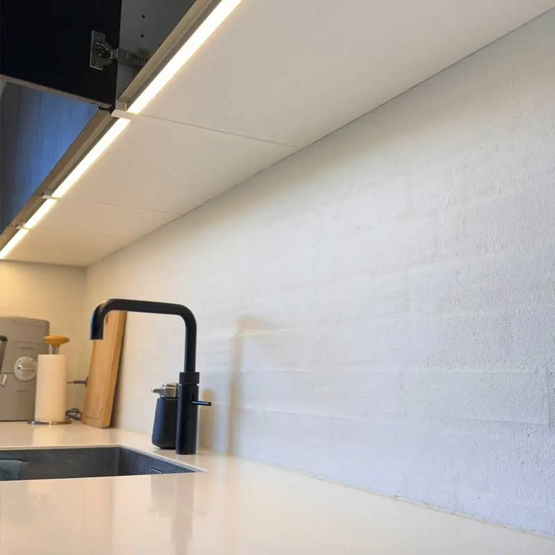 Seamless handleless aluminum Gola profile with integrated LED strip light installed under kitchen wall cabinets, illuminating a white countertop.