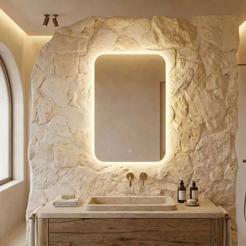 Siena rectangular backlit LED bathroom mirror with rounded corners, emitting a soft warm glow against a natural stone wall texture.